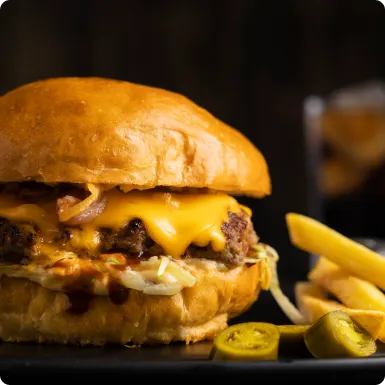 A brioche cheeseburger with melted cheese and onions, served with fries and pickled jalapeños.