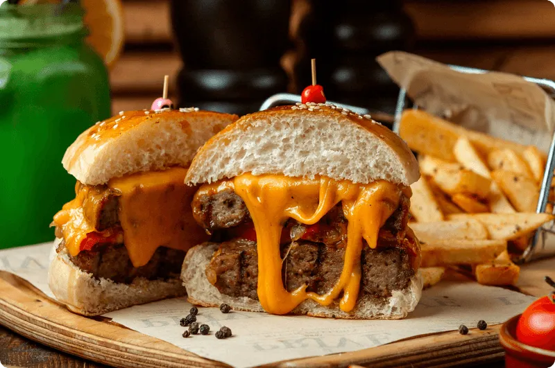 Two thick burgers with melted cheddar running down the sides, served on paper with fries