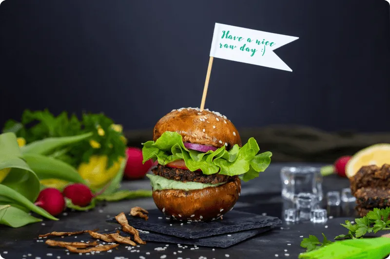 A plant-based burger with lettuce on a slate board, topped with a small flag reading Have a nice veg day
